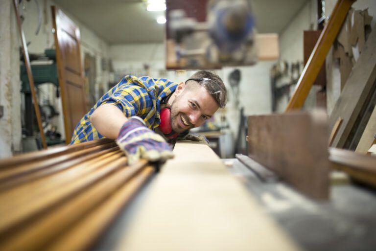 Portrait of experienced carpenter worker cutting wood plank on the machine in his woodworking workshop