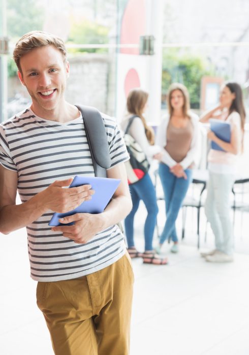 Handsome student smiling and holding tablet at the university